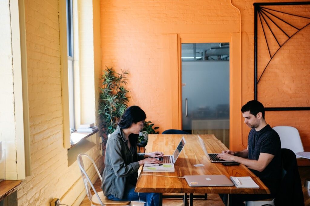 Two professionals at a table with laptops, collaborating on the best proposal management software options.